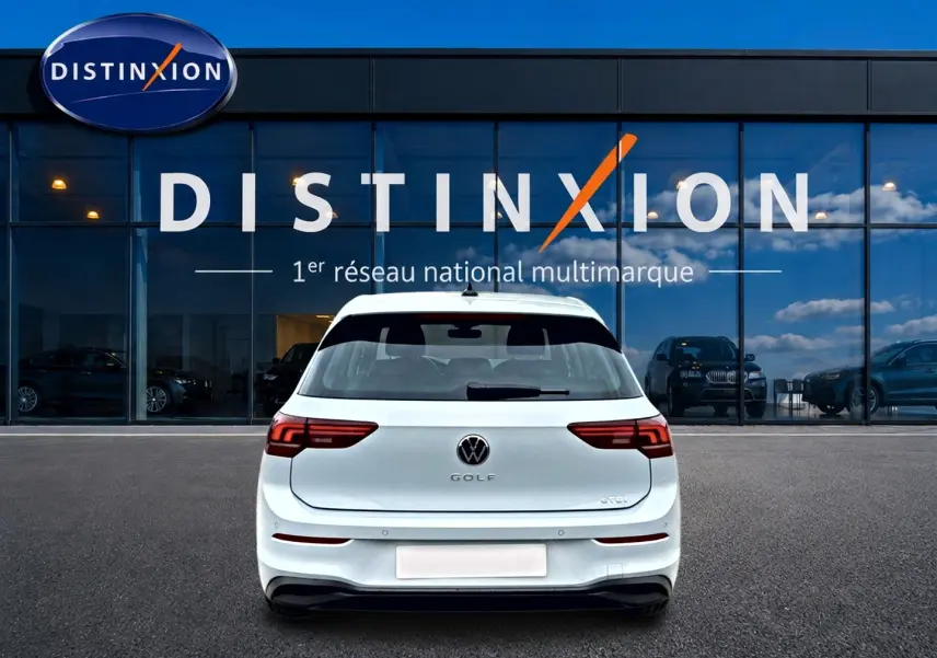 Vue arrière d'une Volkswagen Golf blanche garée devant une vitrine avec le logo Distinxion.