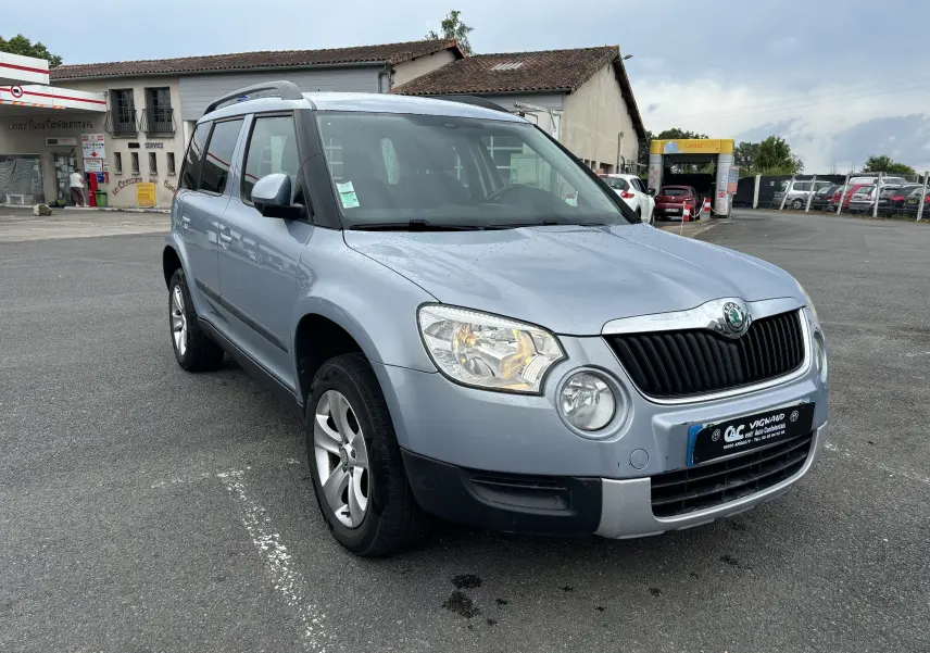 Vue 3/4 avant gauche d'un Skoda Yeti gris 2012 avec toit ouvrant et jantes alliage sur parking.