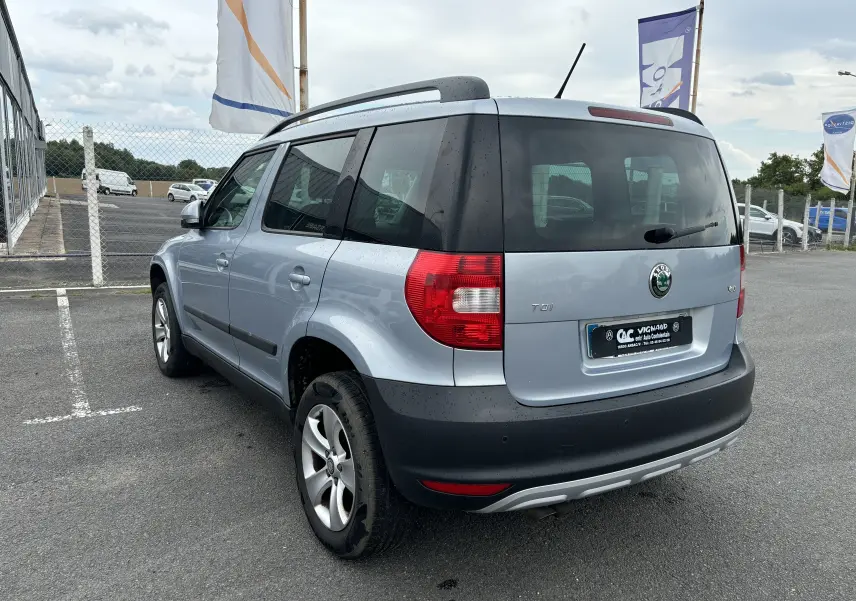 Vue 3/4 arrière droite d'un Skoda Yeti gris 2012 avec jantes alliage et toit équipé de barres de toit.