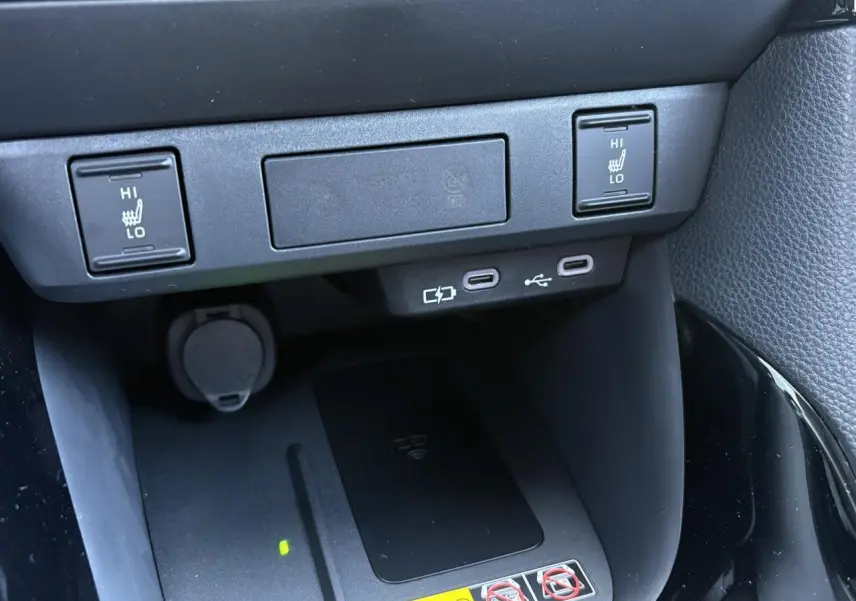 Vue rapprochée de la console centrale de la Toyota Yaris 2025 noire, montrant les commandes des sièges chauffants et le chargeur à induction.