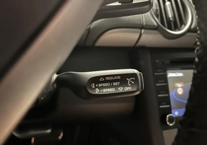 Gros plan sur la commande de régulateur de vitesse à gauche du volant dans l'habitacle noir du Porsche Cayman 987.