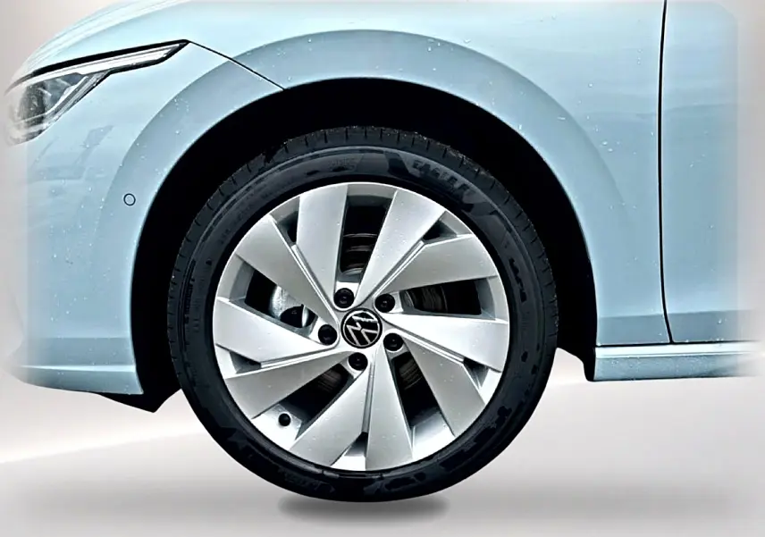 Gros plan sur la roue avant gauche d'une Volkswagen Golf bleu glacier avec jante alu 17 pouces et partie du phare avant visible.