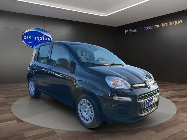 Vue 3/4 avant d'une FIAT Panda noire 2025 avec phares allumés et jantes argentées en showroom.