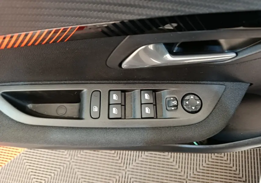 Gros plan sur la commande des vitres électriques et réglages des rétroviseurs côté conducteur d’une Peugeot 208 blanche.