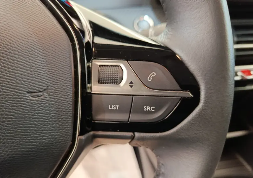Gros plan sur les commandes gauche du volant cuir noir de la Peugeot 208 électrique blanche, boutons liste et appel.