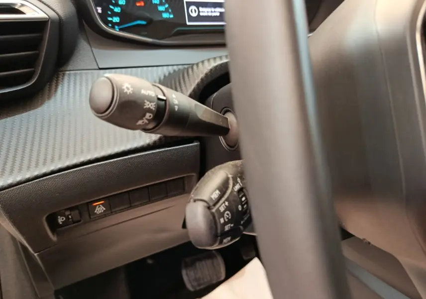 Gros plan sur le volant et les commandes de la Peugeot 208 électrique blanche, tableau de bord digital en arrière-plan.