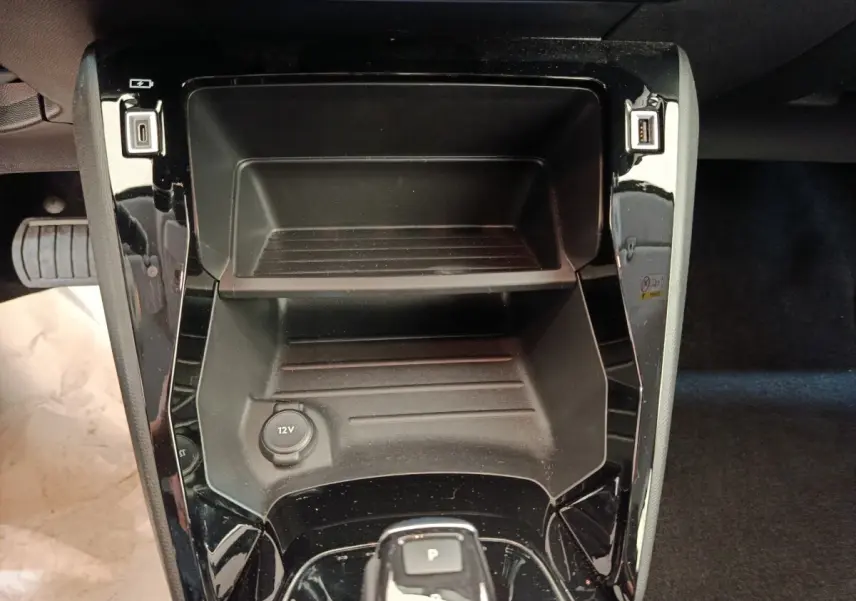 Vue plongeante sur la console centrale noire du Peugeot 208 électrique 2021 avec prise 12V et ports USB.