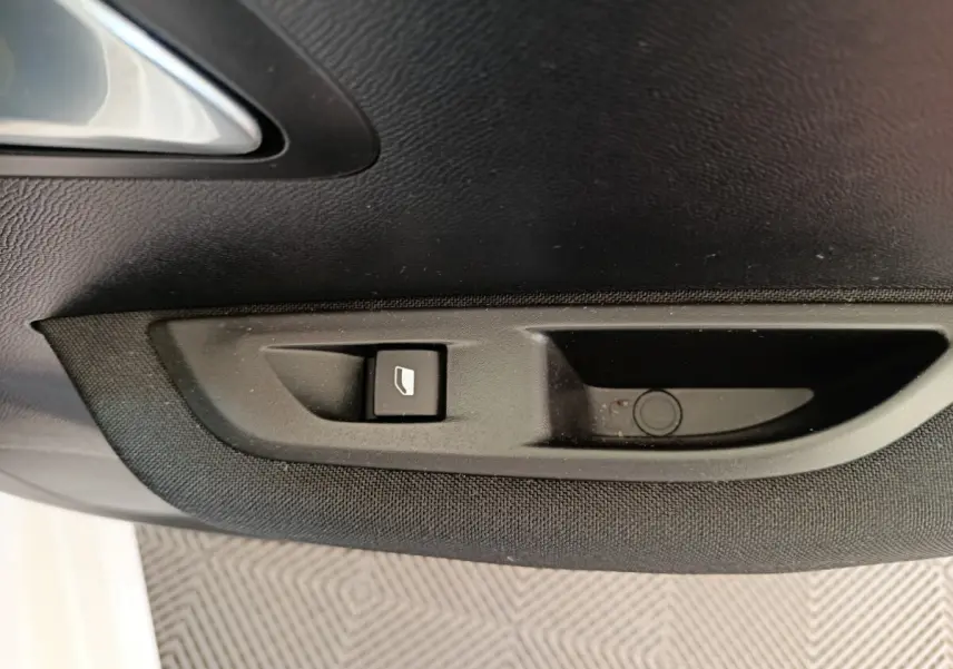Bouton de commande de vitre électrique sur la porte intérieure côté gauche d'une Peugeot 208 électrique blanche.