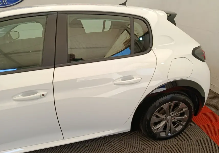 Vue latérale droite sur la partie arrière d’une Peugeot 208 électrique blanche avec jante alliage et porte de recharge visible.