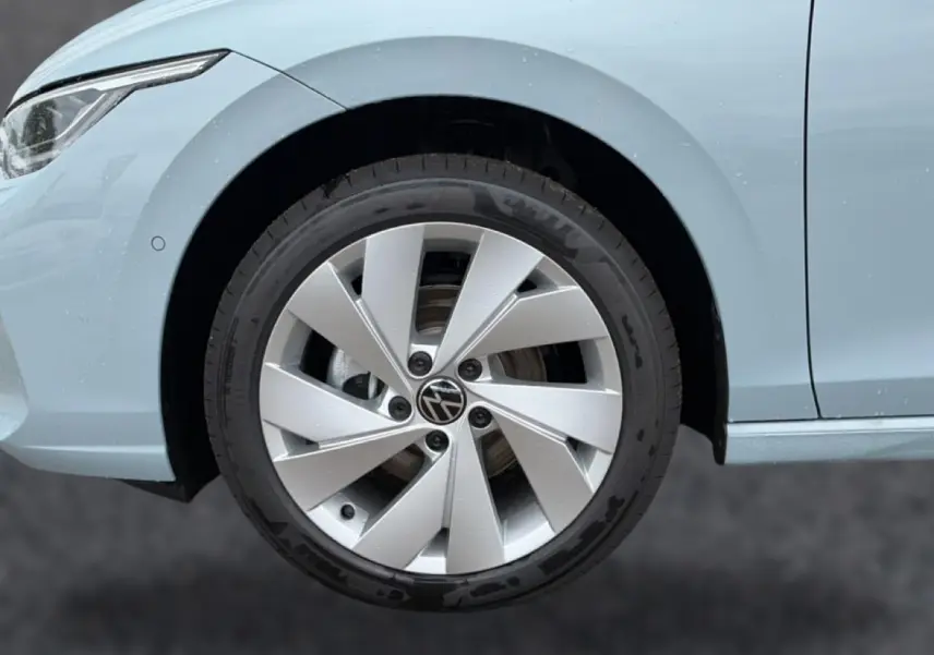 Gros plan sur la roue avant gauche d’une Volkswagen Golf bleu glacier avec jante alu 17 pouces au design moderne.