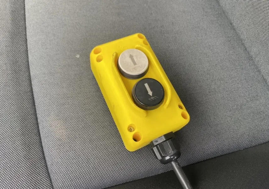 Télécommande jaune de commande de benne posée sur un siège gris à l'intérieur du Renault Master blanc.