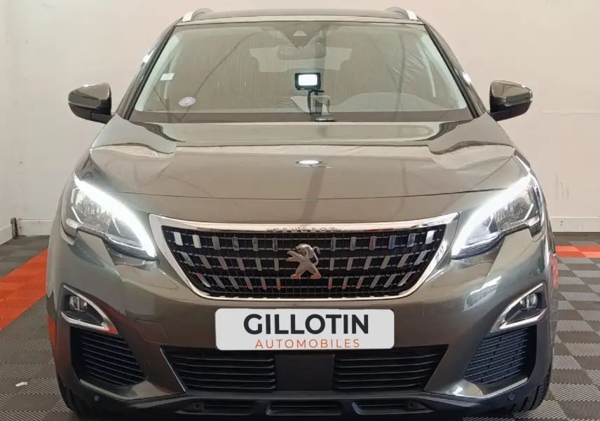 Vue de face du Peugeot 3008 gris foncé avec phares LED allumés et calandre chromée distinctive.