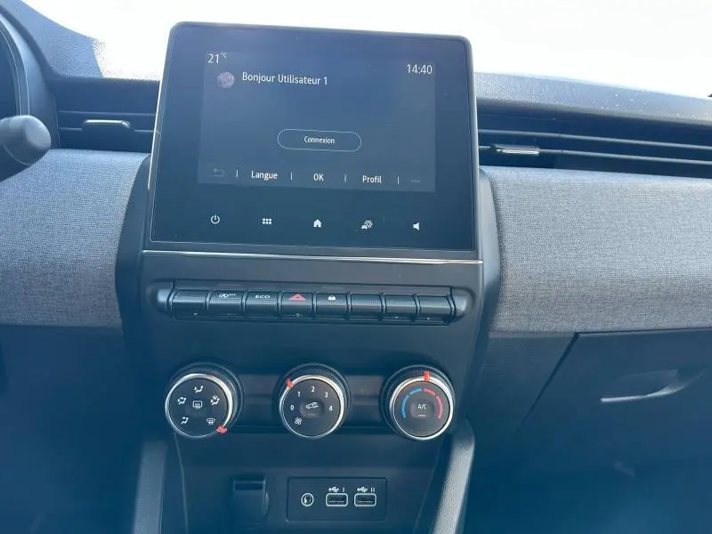 Tableau de bord de Renault Clio 2025 avec écran tactile, commandes clim manuelle et tissu gris motif 3D visible.