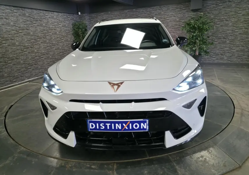 Vue avant d'une CUPRA Formentor blanche avec phares allumés et calandre noire dans un showroom intérieur.