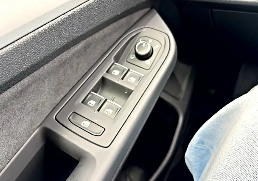 Gros plan sur la commande des vitres côté conducteur d’une Volkswagen Golf noire, intérieur tissu gris.