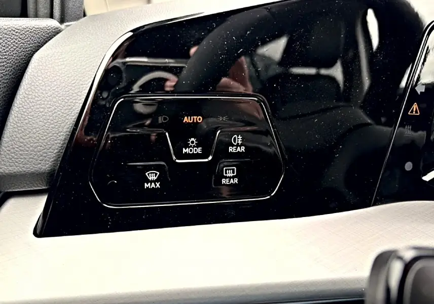 Gros plan sur les commandes de phares automatiques et de désembuage du tableau de bord noir de la Volkswagen Golf 2026.