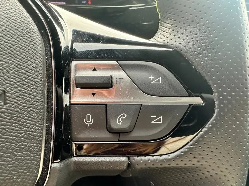 Gros plan sur les commandes du volant multifonction noir perforé de la Peugeot 308 SW 2023, version GT.