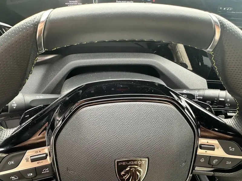 Gros plan sur le volant noir perforé avec surpiqûres jaunes du Peugeot 308 SW 2023, mettant en valeur les commandes intégrées.