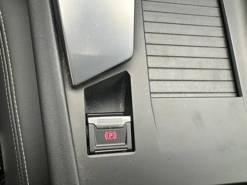 Gros plan sur le bouton de frein de stationnement électrique rouge, console centrale noire du Peugeot 308 SW 2023.