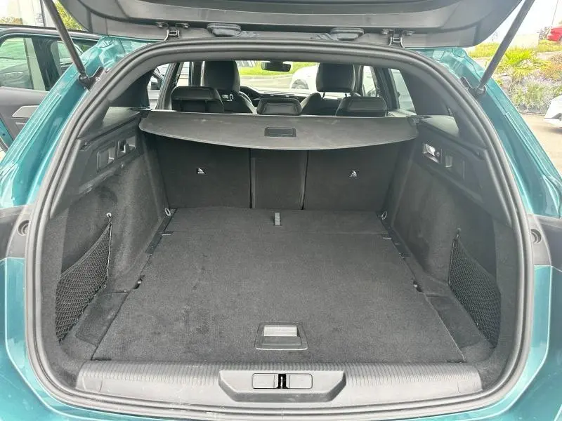 Coffre ouvert vue arrière d’un Peugeot 308 SW vert avec cache-bagages et banquette arrière noire.