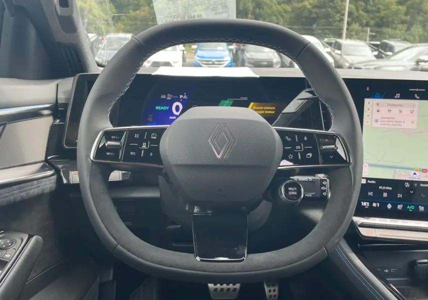 Vue centrée sur le volant en cuir noir avec logo Renault, tableau de bord numérique et écran tactile du Renault Austral gris schiste.