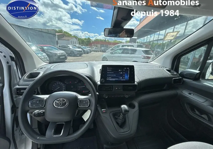 Vue intérieure avant du Toyota Proace City 2023 blanc, montrant le volant, la console centrale avec écran tactile et la boîte manuelle.