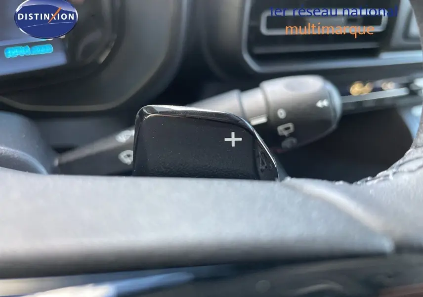 Gros plan sur la palette de changement de vitesse "+" derrière le volant d'un Citroën Berlingo noir, intérieur moderne.
