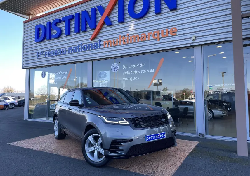 Range Rover Velar D240 S R-Dynamic gris Corris en 3/4 avant droit devant un showroom Distinxion.