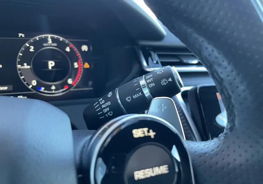 Gros plan sur le volant perforé et la commande de régulateur de vitesse du Range Rover Velar gris côté conducteur.