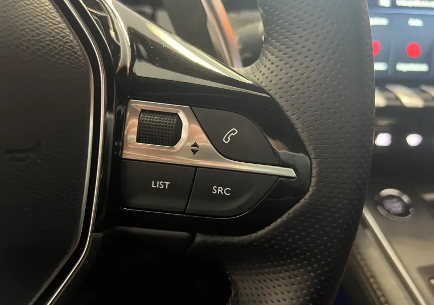 Gros plan sur les commandes du volant côté gauche d'une Peugeot 508 SW 2024, cuir perforé noir et touches fonctionnelles.