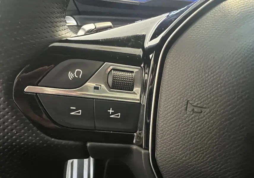 Gros plan sur les commandes vocales et volume du volant cuir perforé de la Peugeot 508 SW 1.5 HDI GT blanche 2024