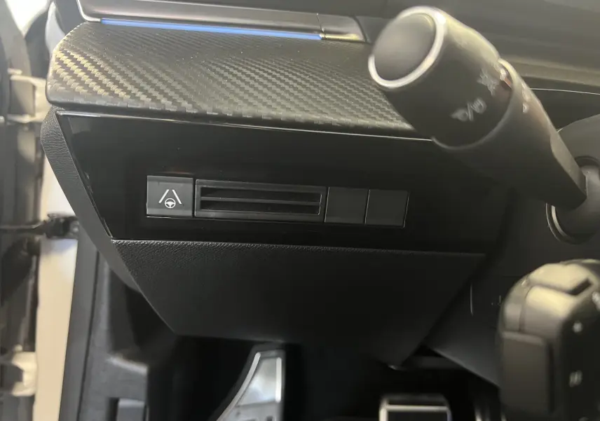 Détail du tableau de bord côté gauche avec finition carbone et commandes d'assistance sur Peugeot 508 SW blanc 2024