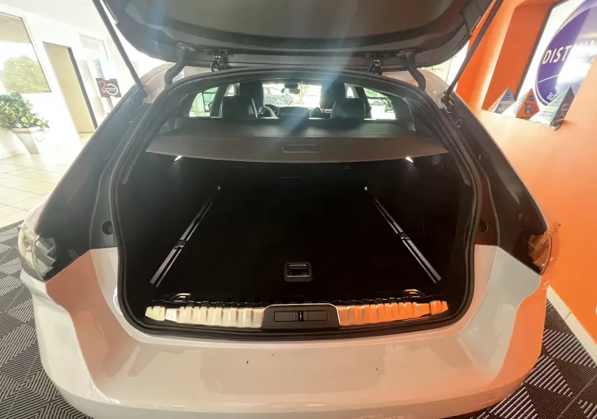 Coffre ouvert vu de l'arrière d'une Peugeot 508 SW blanche 2024, montrant l'espace de chargement et la plage arrière.