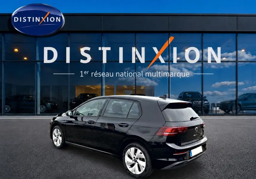 Vue 3/4 arrière droite d'une Volkswagen Golf noire 2026 garée devant une vitrine Distinxion.