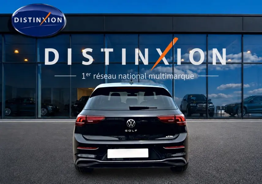 Vue arrière d'une Volkswagen Golf noire 2026 garée devant une vitrine avec logo Distinxion visible.