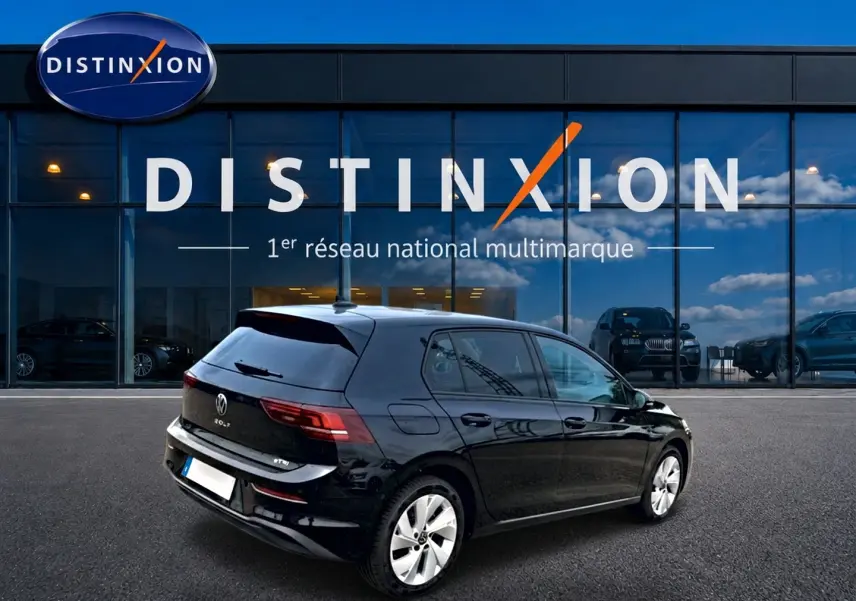Vue 3/4 arrière droite d'une Volkswagen Golf 1.5 ETSI Evo2 noire garée devant une vitrine Distinxion.