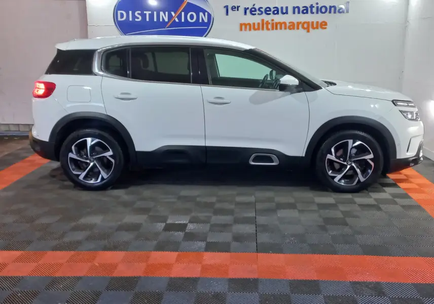 Profil droit d'un SUV Citroën C5 Aircross blanc, avec jantes alliage bicolores et feux arrière allumés en intérieur showroom.