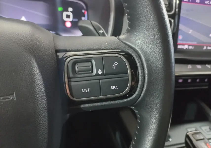 Gros plan sur les commandes gauche du volant cuir noir d'une Citroën C5 Aircross 2020 avec écran tactile en arrière-plan.