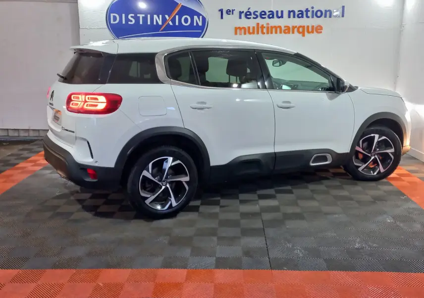 Vue de profil côté gauche d'un Citroën C5 Aircross blanc avec feux arrière allumés dans un showroom.