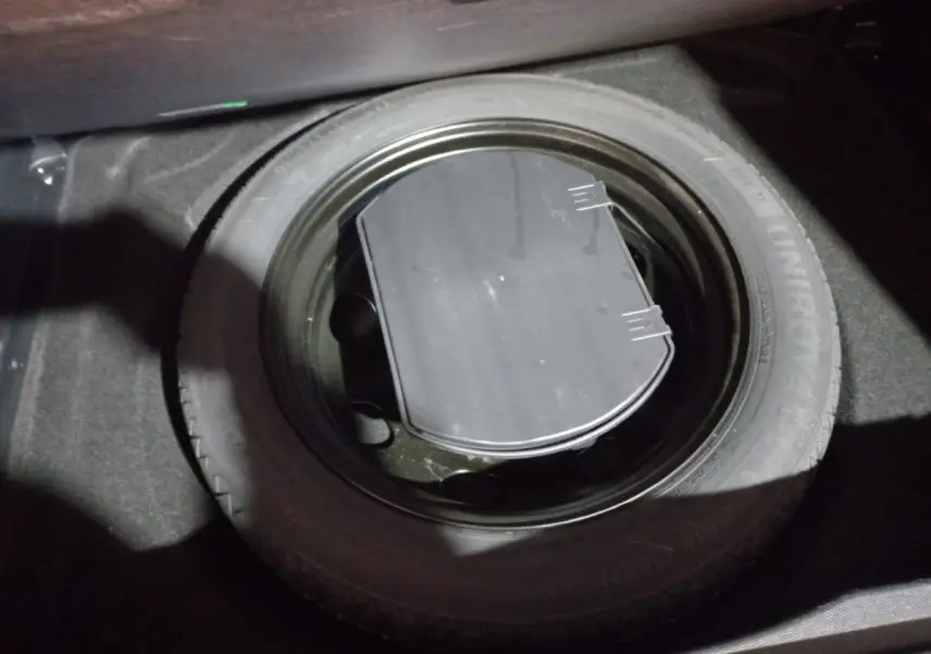 Gros plan sur la roue de secours noire dans le coffre d'un Citroën C5 Aircross blanc, vue intérieure depuis le dessus.