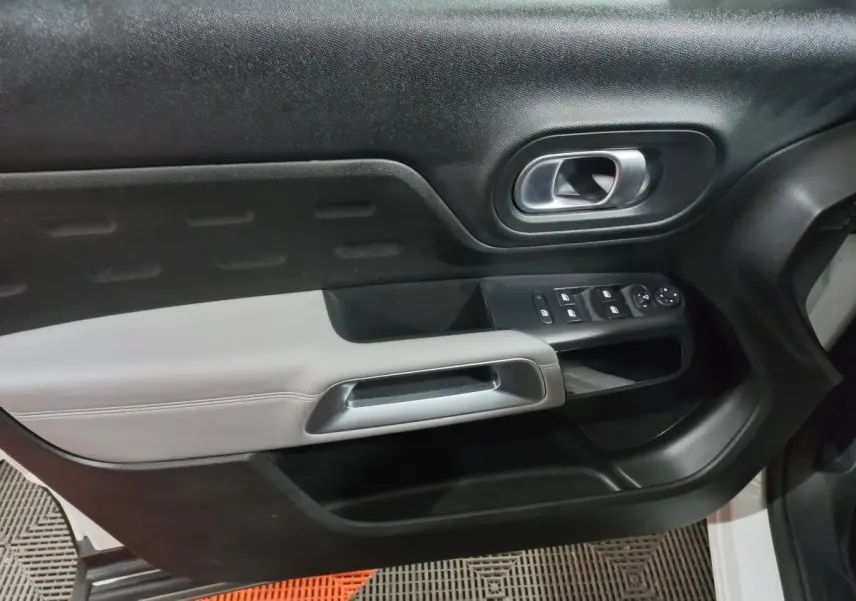 Gros plan sur la porte avant droite intérieure du Citroën C5 Aircross blanc, avec commandes électriques et poignée argentée.
