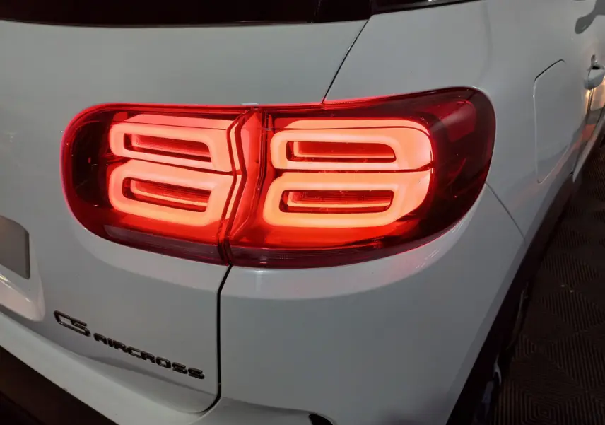 Gros plan sur le feu arrière droit rouge allumé d'un Citroën C5 Aircross blanc, avec logo visible sur la carrosserie.