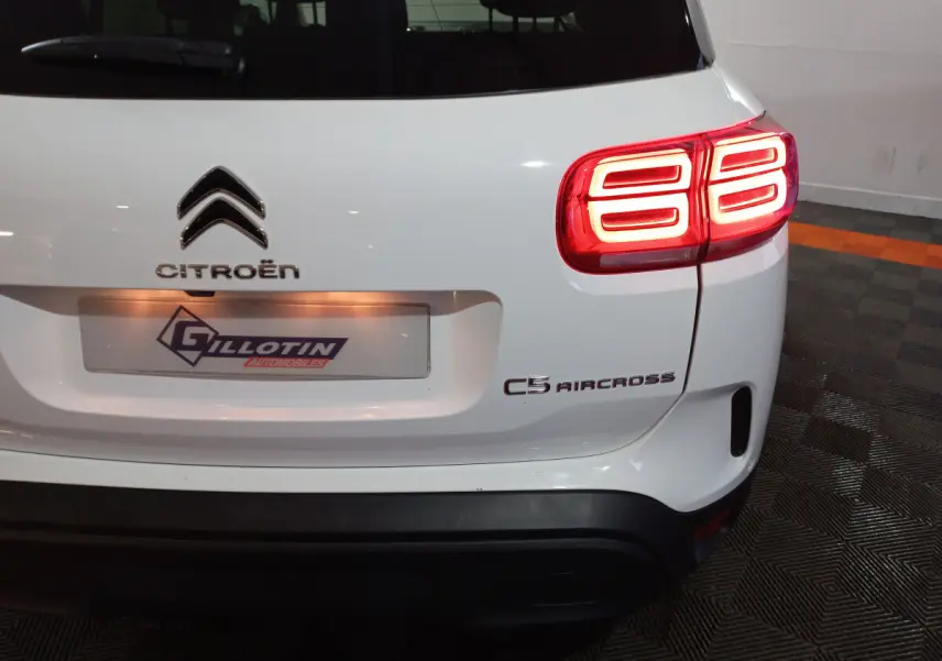 Vue arrière droite d'un Citroën C5 Aircross blanc avec feux arrière allumés et logo visible sur un sol carrelé.