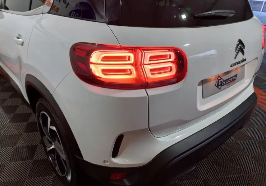 Vue 3/4 arrière gauche d'un Citroën C5 Aircross blanc avec feux arrière LED allumés et logo Citroën visible.