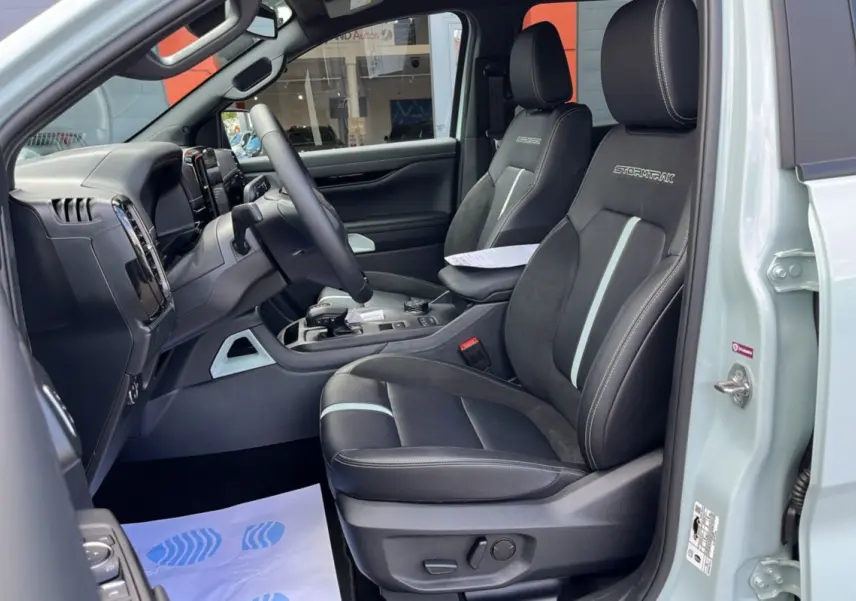 Vue intérieure côté conducteur du Ford Ranger gris zen 2026, sièges noirs Stormtrak avec surpiqûres blanches et volant multifonctions.