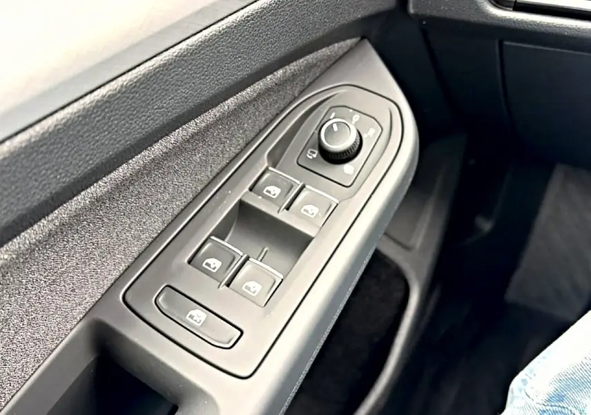 Gros plan sur les commandes électriques des vitres et rétroviseurs côté conducteur d'une Volkswagen Golf bleu glacier.