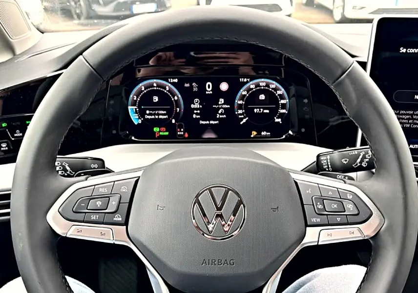 Vue rapprochée du volant noir d'une Volkswagen Golf 2026 avec tableau de bord digital et commandes intégrées.