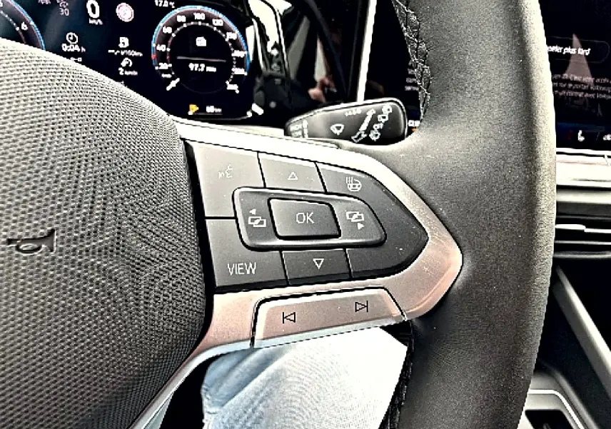 Gros plan sur le volant multifonction noir de la Volkswagen Golf 2026 avec commandes et tableau de bord numérique en arrière-plan.