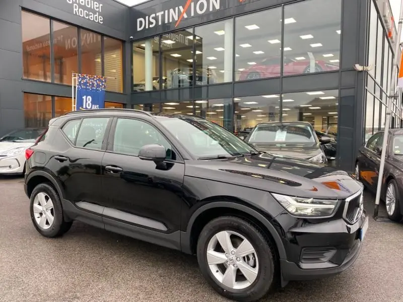 Vue 3/4 avant droite d'un Volvo XC40 T3 noir solid garé devant une concession Distinxion, avec jantes argentées visibles.