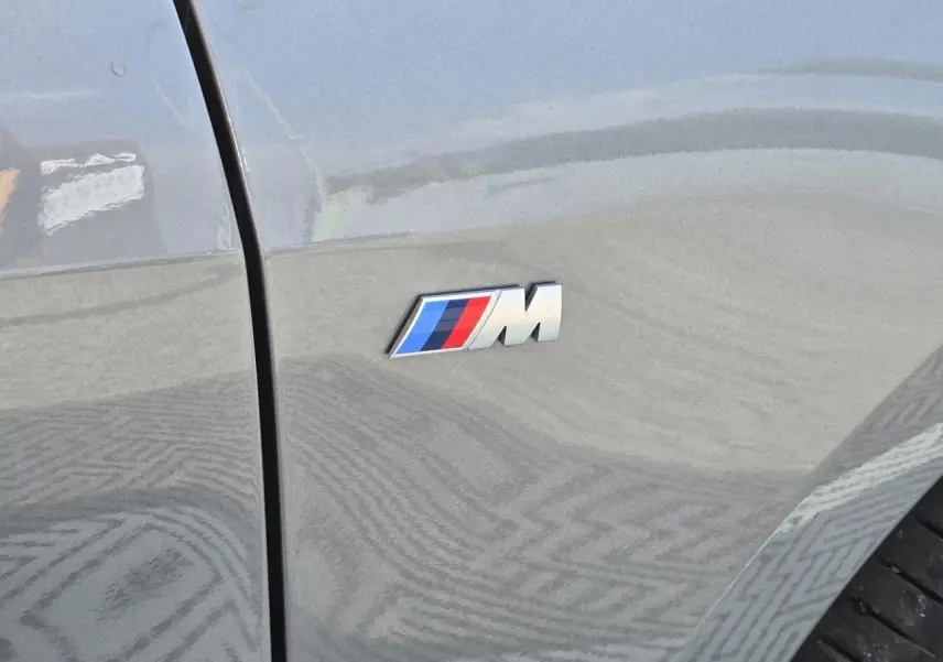 Gros plan sur l'emblème M sur l'aile avant droite d'une BMW Série 1 gris Skyscraper 2024.